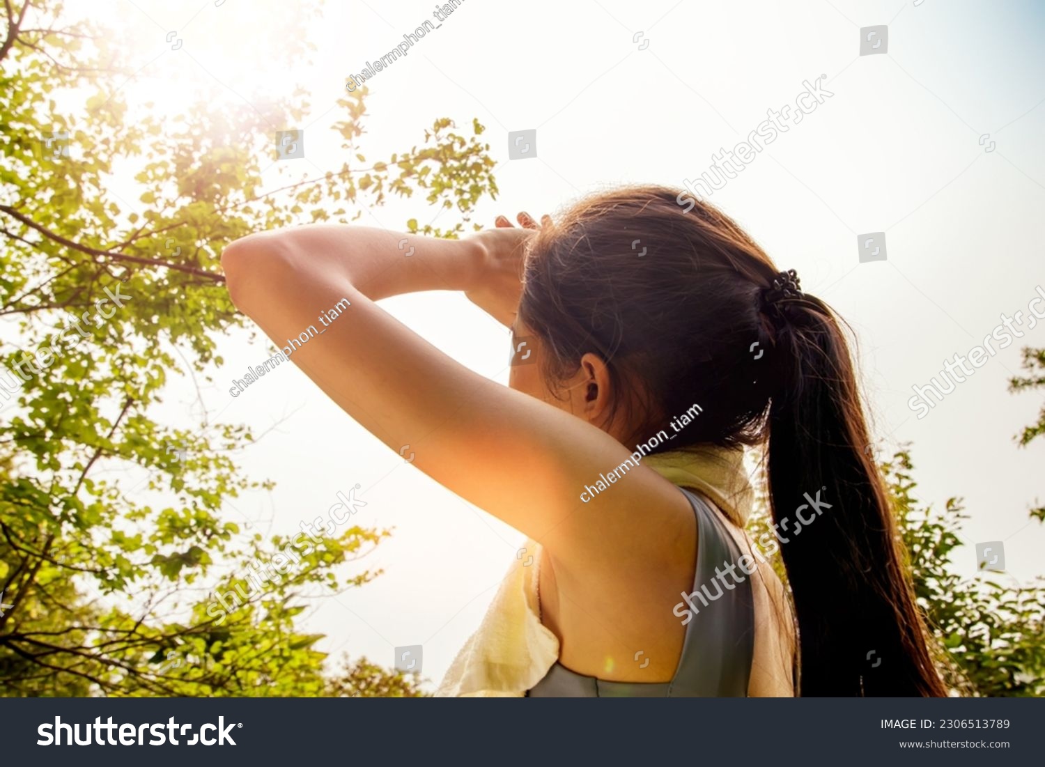 Back view Asian woman doing sport jogging feeling sun and heat too hot during jogging in park sweltering summer weather covering face with hands covering face against UV rays. #2306513789
