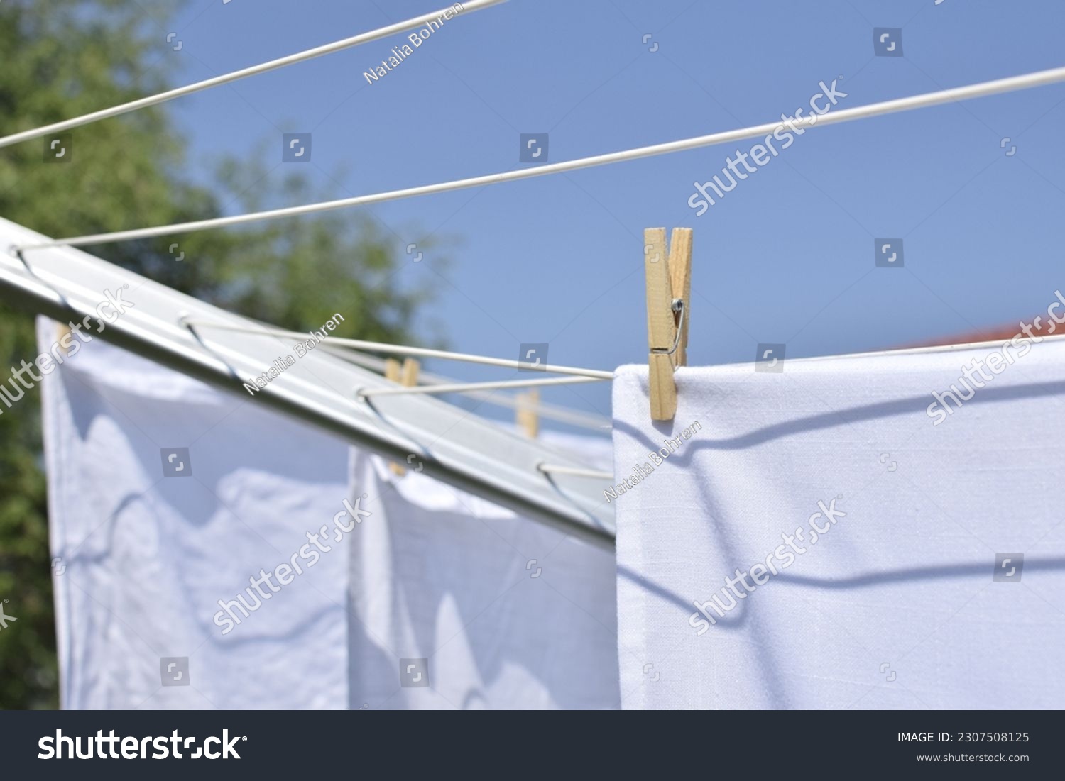 A wooden clothespin holds white laundry on a clothesline outdoors. #2307508125