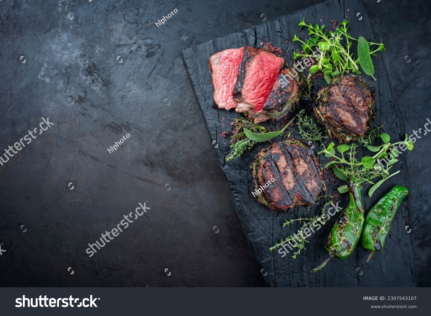 Traditional barbecue dry aged angus medaillon beef filet steak natural with herbs and red wine salt served as top view on a charred wooden board with copy space left  #2307543107