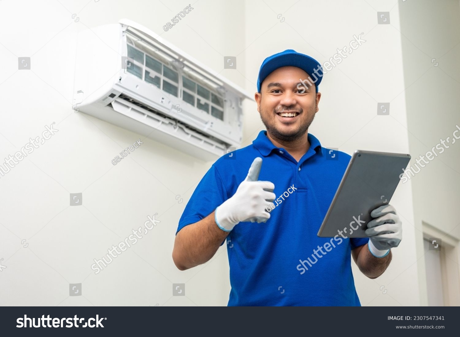 Technician in uniform using tablet to check list of maintenance and cleaning filters of air conditioner. Air condition maintenance service. Home services concept. #2307547341