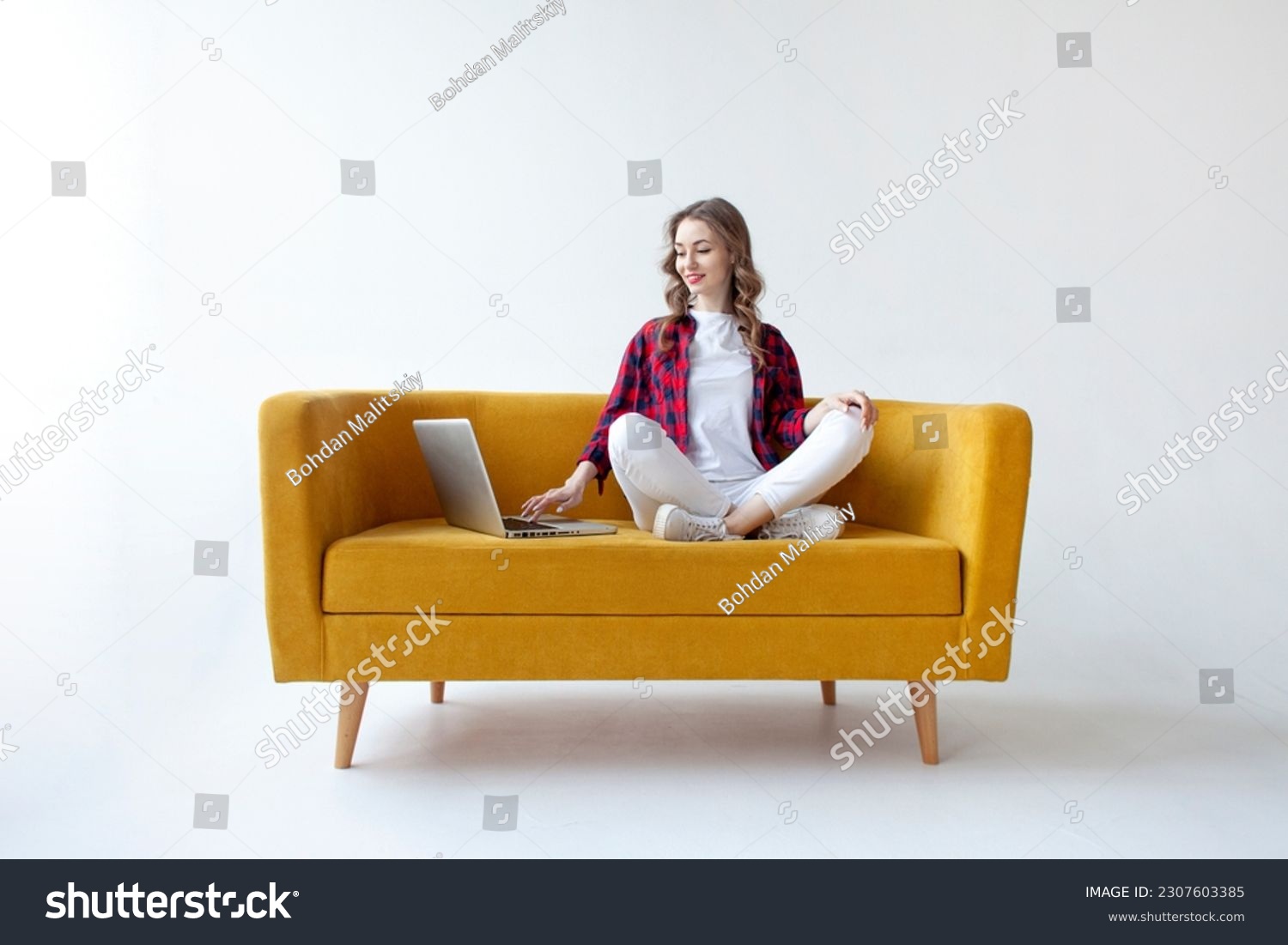 young cute girl uses laptop on comfortable soft sofa, woman types online on computer on yellow couch on white isolated background #2307603385