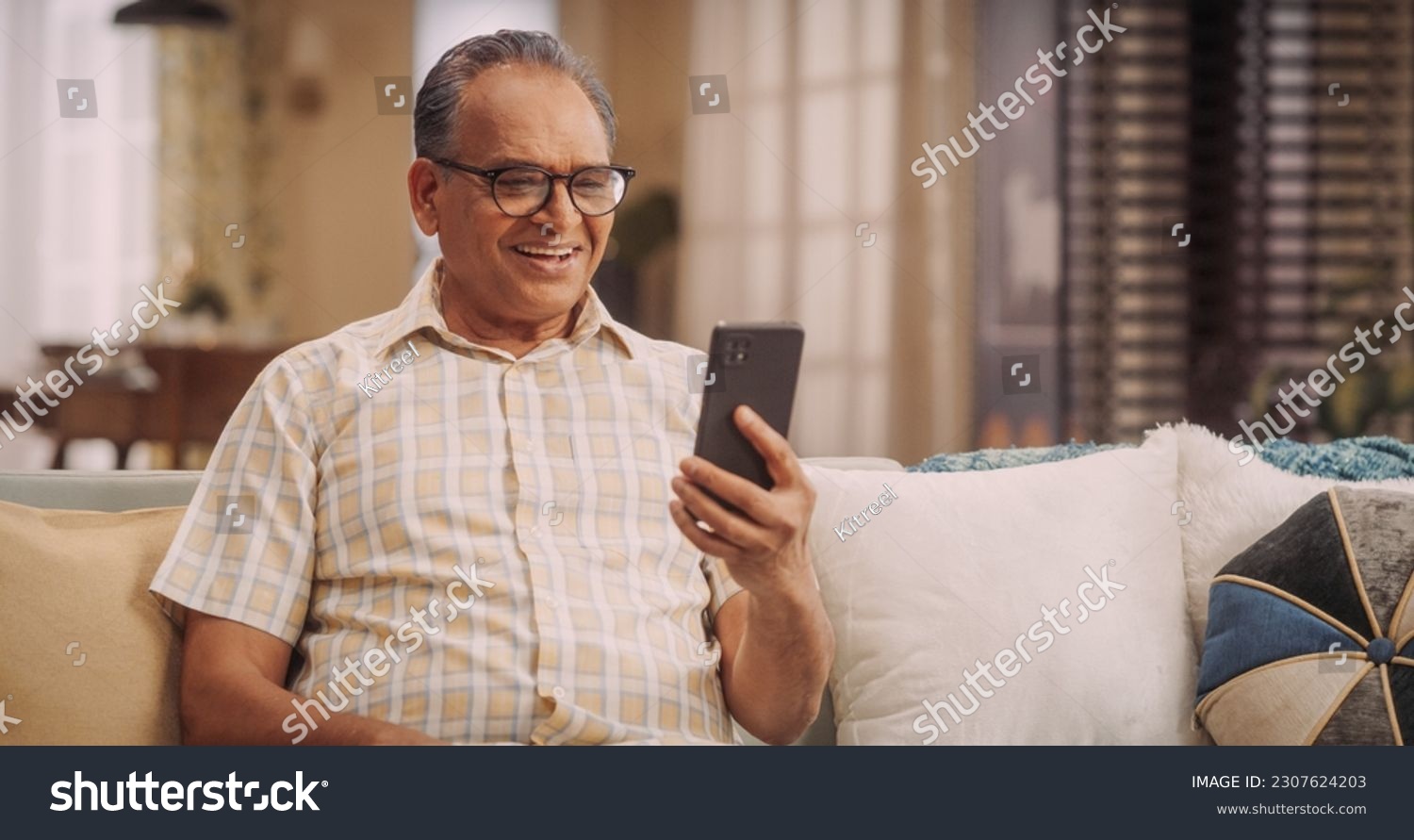 Elderly Indian Man Using Phone for Video Call, Smiling and Happy: Talking with Old Friends and Sharing Life Updates. Cherishing Meaningful Conversations and Laughter with Family Remotely #2307624203