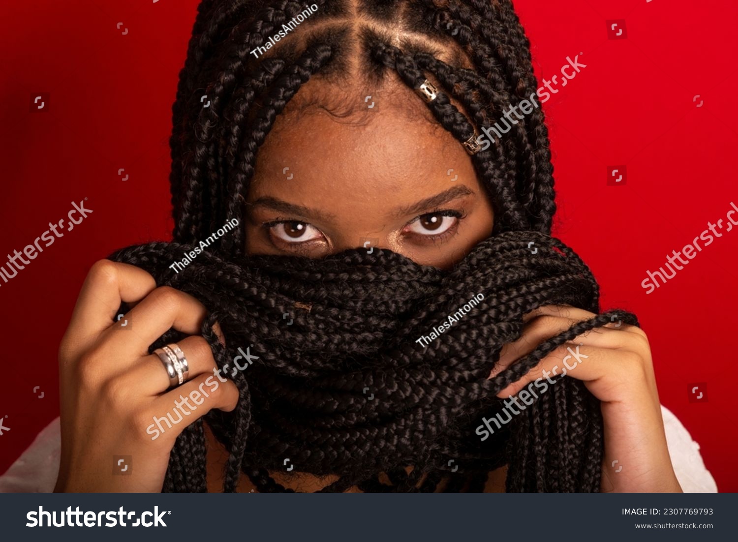 Close-up portrait of black woman with holding her braids to her face. Isolated on red background #2307769793