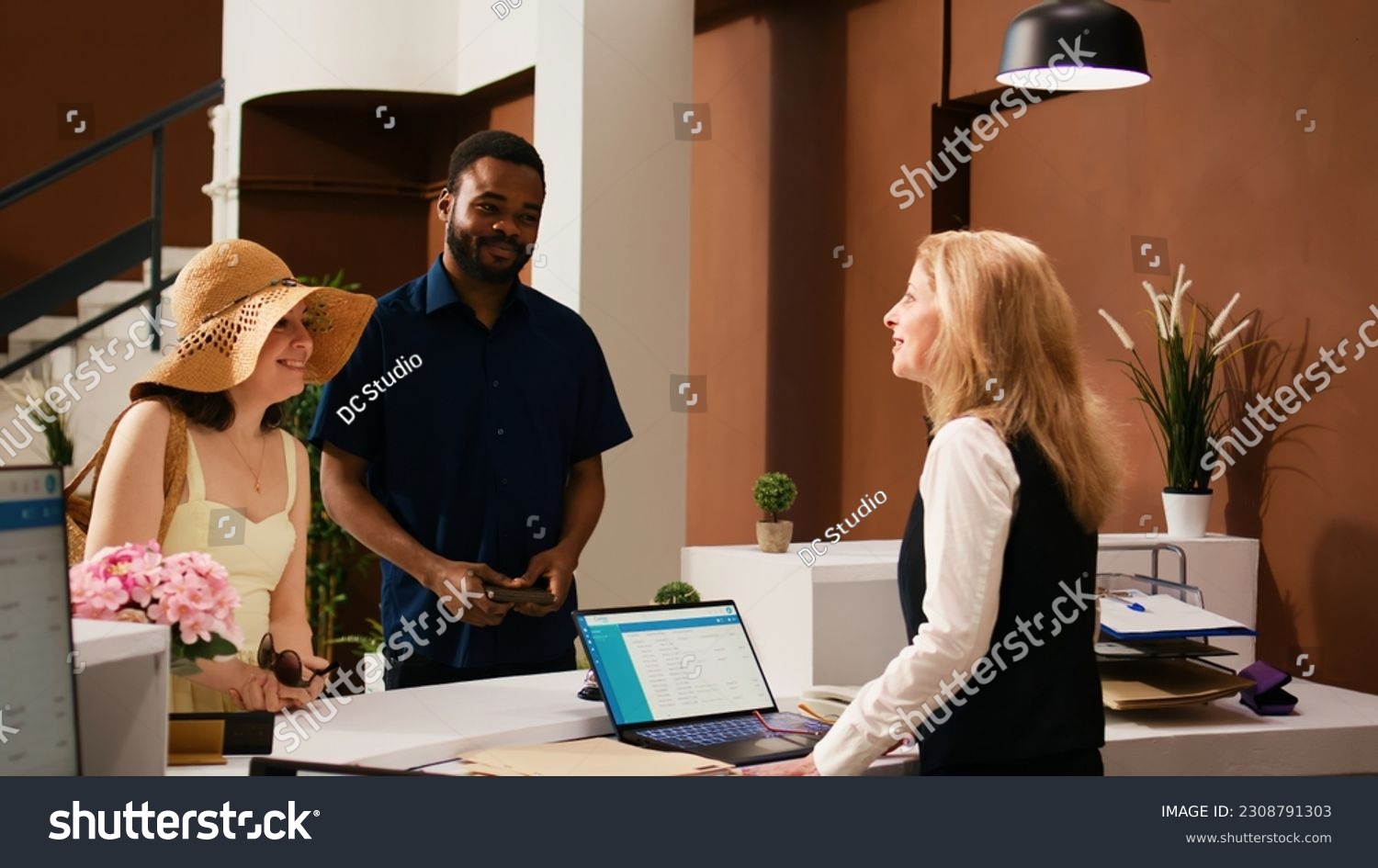 Hotel concierge greeting tourists at reception upon their arrival, welcoming guests at luxury tropical resort. Receptionist preparing to check in guests, providing excellent service. #2308791303