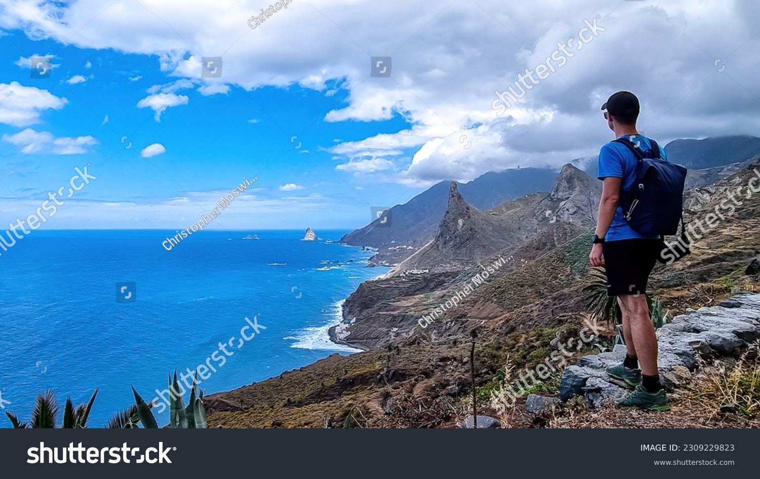 Backpack man with scenic view of Atlantic Ocean coastline and Anaga mountain range on Tenerife, Canary Islands, Spain, Europe. Looking at Roque de las Animas crag. Hiking trail from Afur to Taganana #2309229823