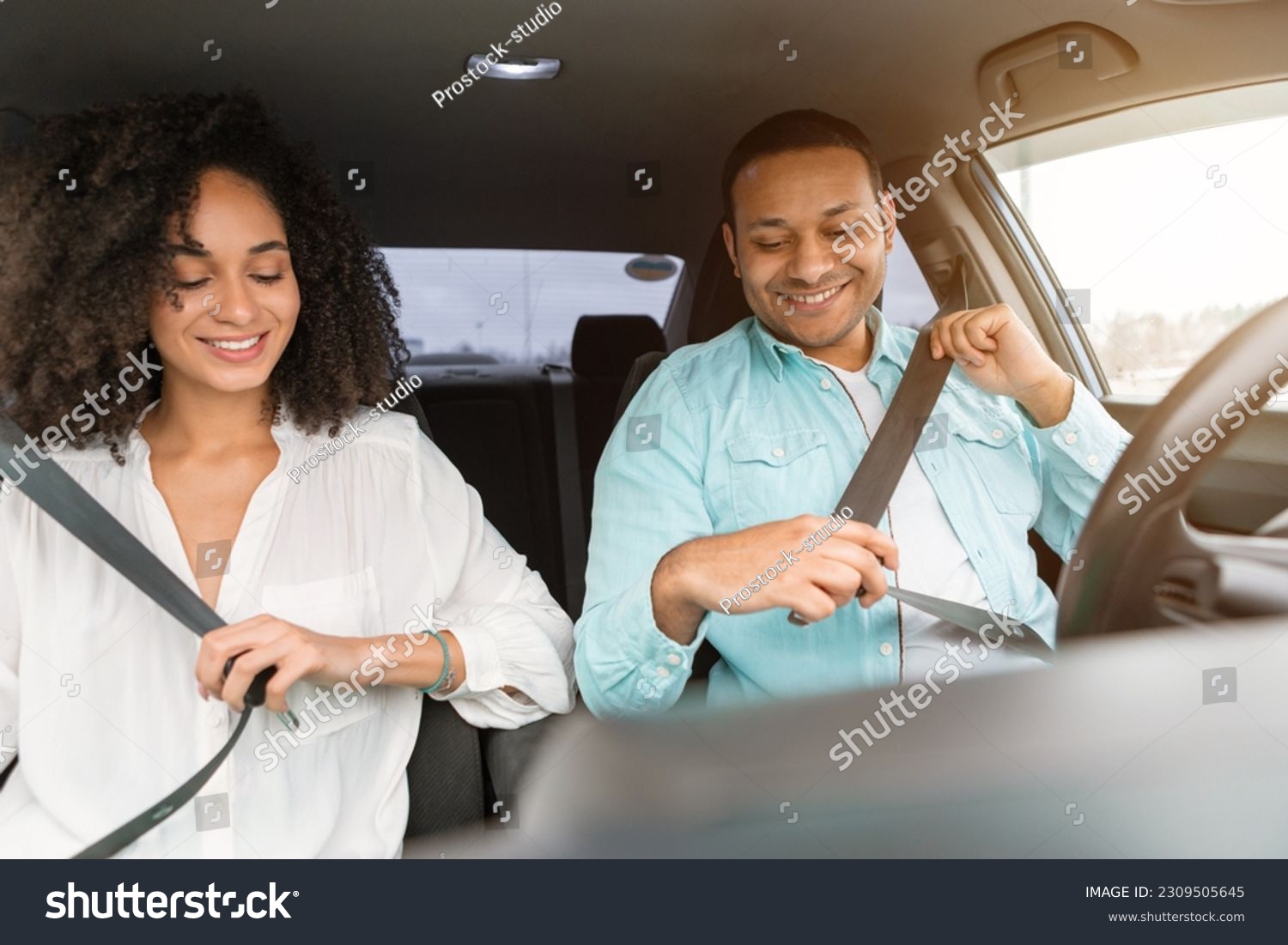 Road Safety Concept. Middle eastern couple practicing safe driving habits, wearing seat belts sitting in new car inside, enjoying comfort of vehicle. Safe Transportation And Auto Insurance Offer #2309505645