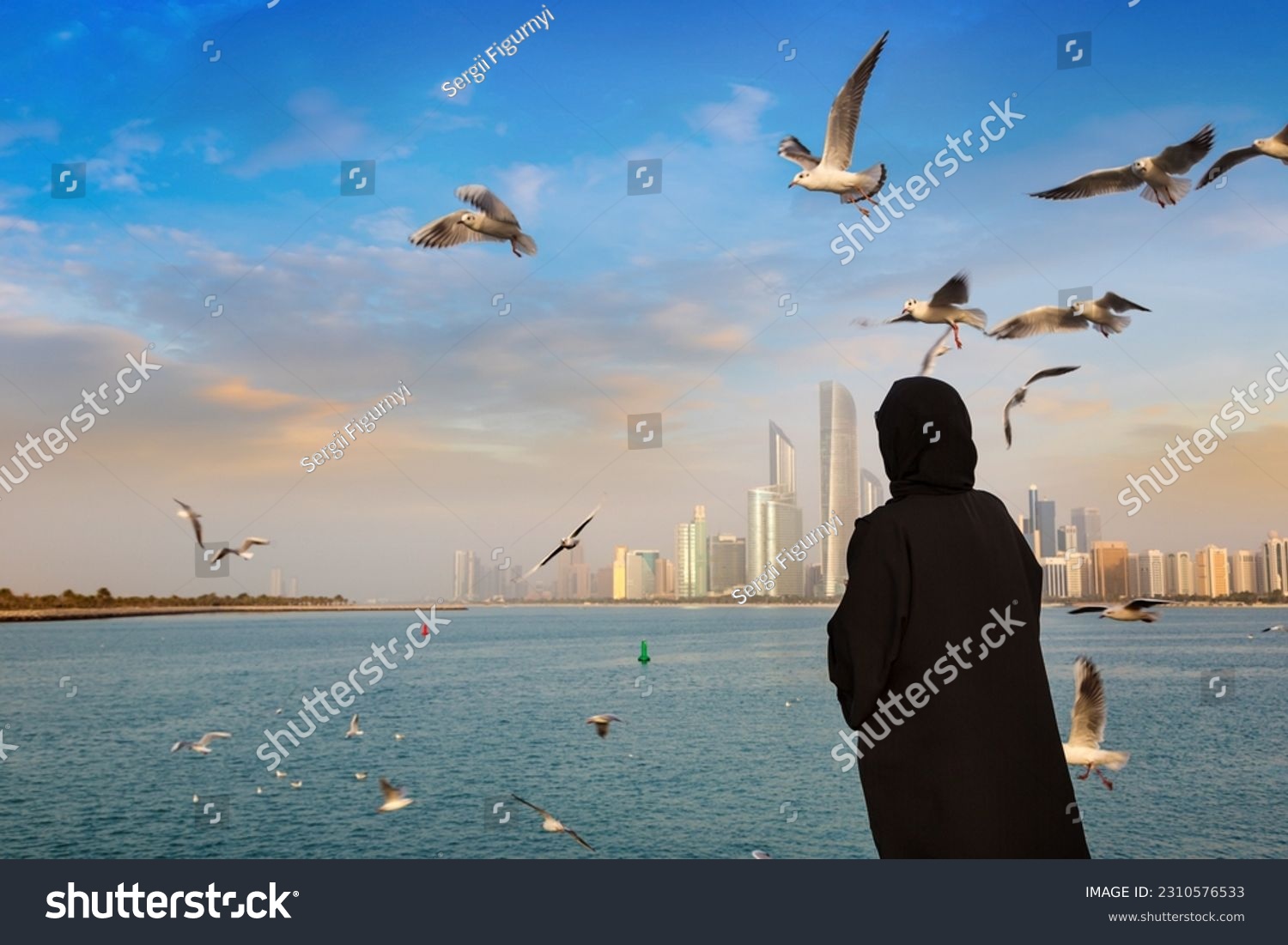 A woman wearing arab clothes is feeding seagulls in Abu Dhabi in a summer day, United Arab Emirates #2310576533