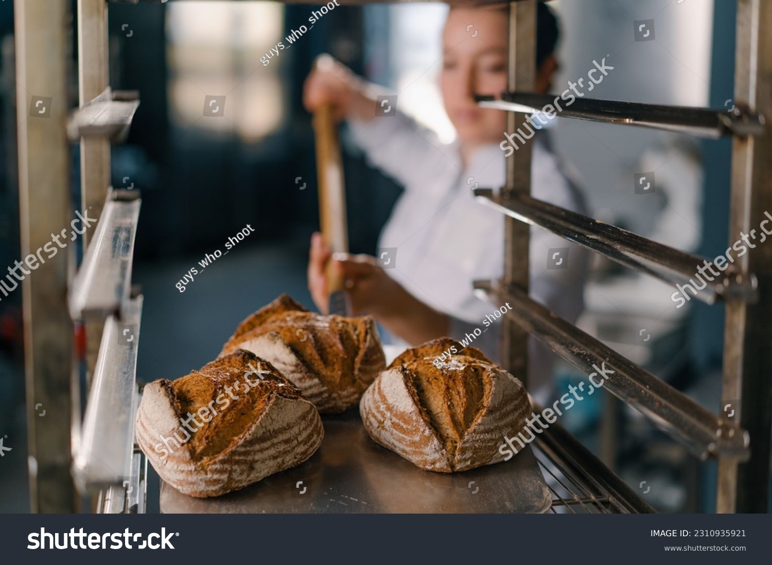 female baker takes out freshly baked fresh bread from the oven and puts it on the shelf in kitchen of the bakery Culinary profession #2310935921