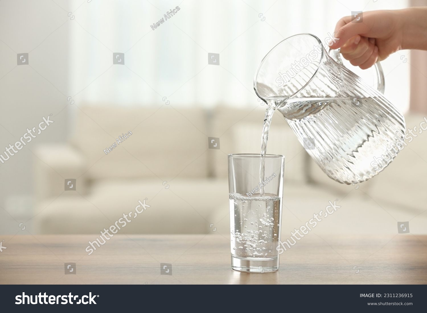 Woman pouring water from jug into glass at table indoors, closeup. Space for text #2311236915