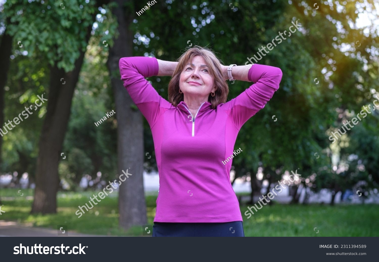 Portrait of beautiful senior woman looking at camera and smiling while standing in forest #2311394589