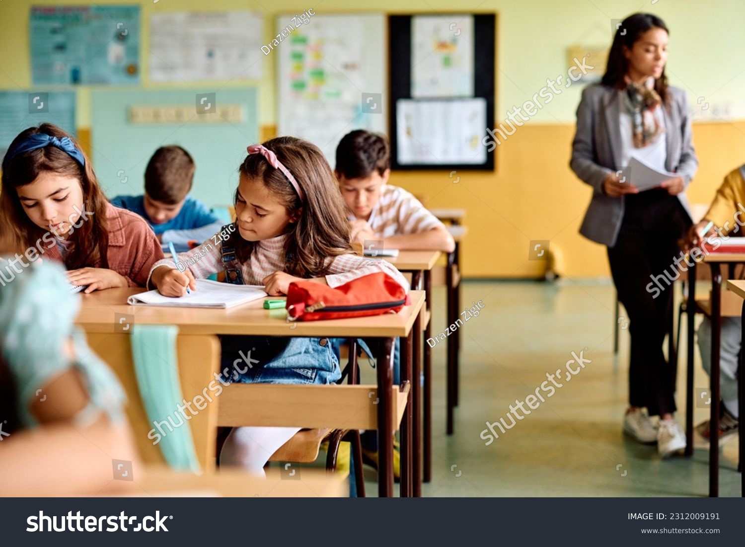 Group of elementary students having an exam at school. Focus is on Hispanic girl writing in her notebook. #2312009191