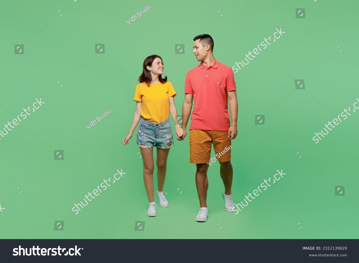 Full body happy smiling young couple two friends family man woman wear basic t-shirts together walk going hold hands look to each other isolated on pastel plain light green background studio portrait #2312139829