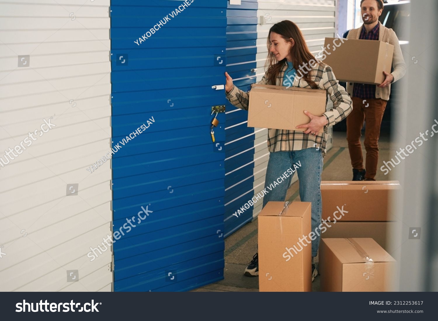 Woman and man with big cardboard boxes into warehouse with self storage unit #2312253617