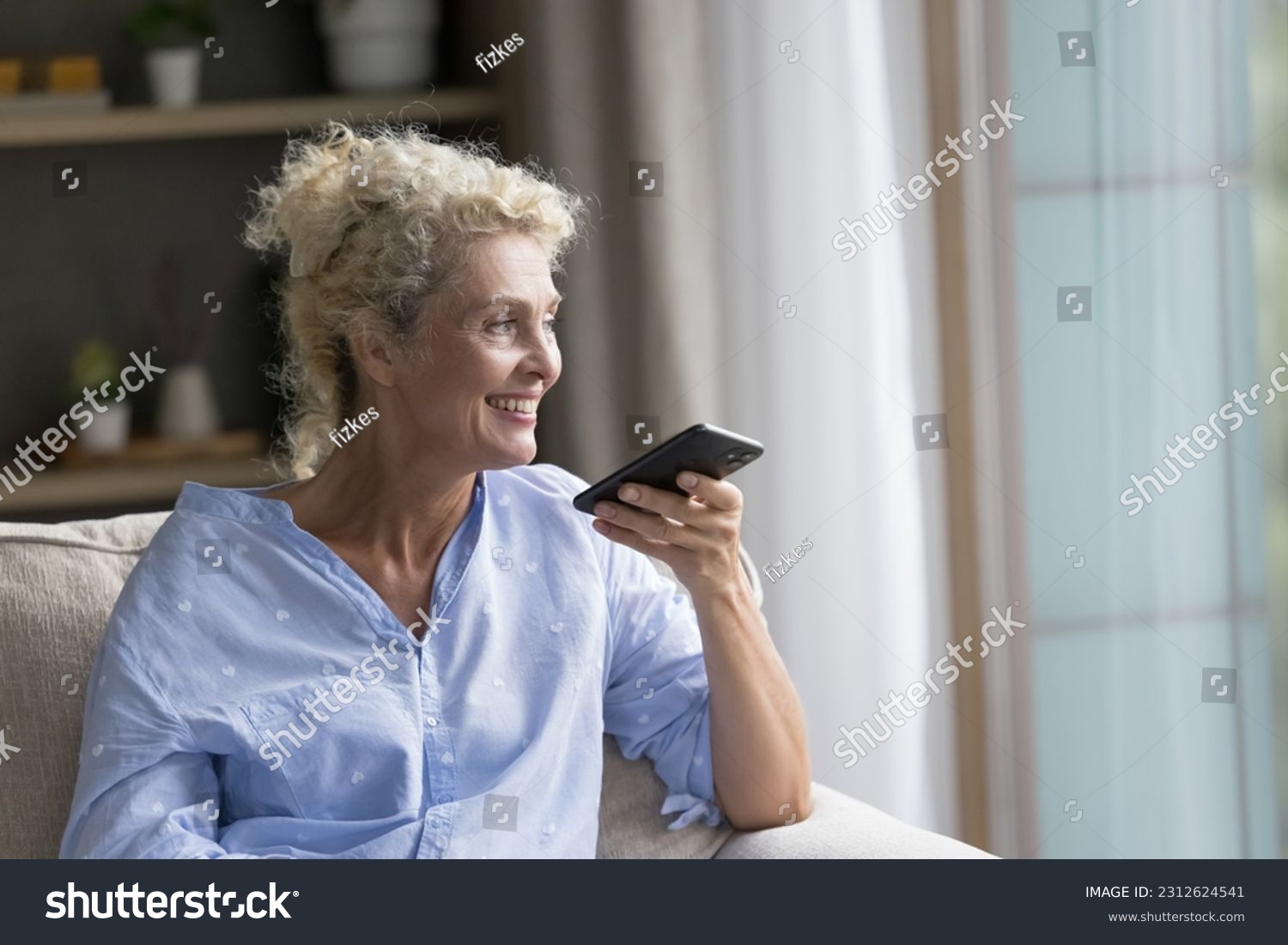 Happy senior mature lady talking on speaker on cellphone call, speaking at dynamic, holding smartphone at face, recording audio message, resting at home, smiling, laughing, enjoying communication #2312624541
