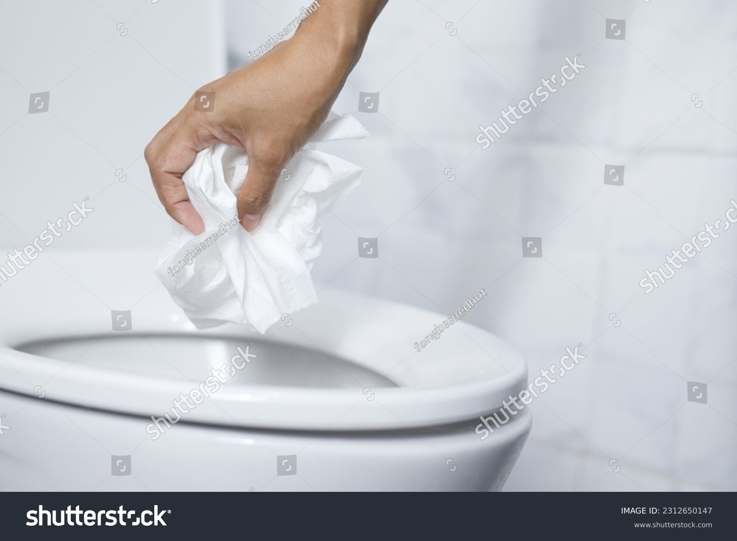 close up hand holding a tissue to be thrown into the toilet bowl. Can not drain water of toilet paper in the toilet bowl cause the stool to clog up. #2312650147