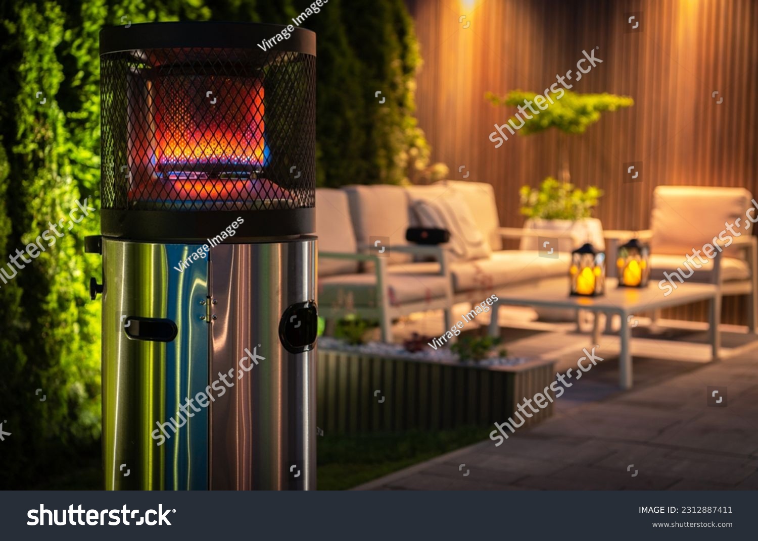 Outdoor Patio Propane Gas Heater For Cold Evenings in Garden Area. Burning Heater in Front of Outdoor Relaxing Area During Night Time. #2312887411