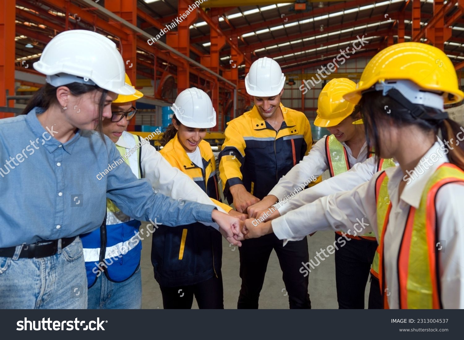 Group of male and female factory labor bumping fist together after finish meeting. Everyone wearing safety uniform and helmet. Workers working in the metal sheet factory. #2313004537