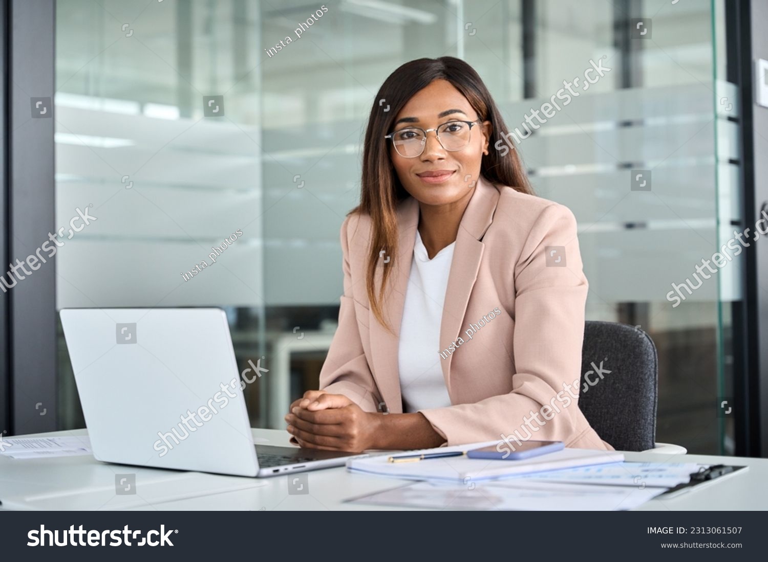 Confident young female lawyer, professional African American business woman company manager executive wearing suit glasses working on laptop in office sitting at desk looking at camera, portrait. #2313061507