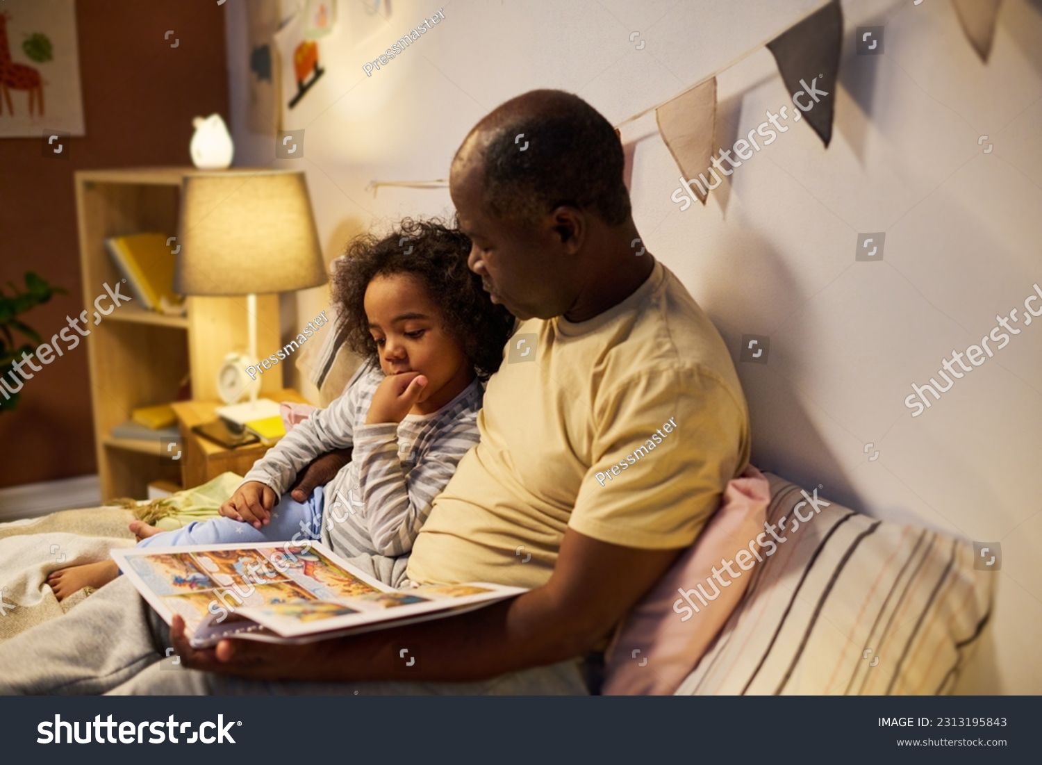 African American dad reading fairy tale to his child, they sitting on bed and watching pictures in book #2313195843