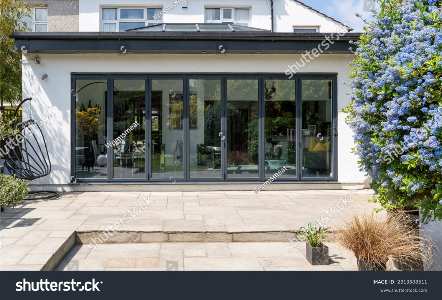 Stylish, closed, bifold doors with plants in spring, summer, revealing interior of a designer, lifestyle, kitchen diner room. Indian sandstone patio. #2313508511