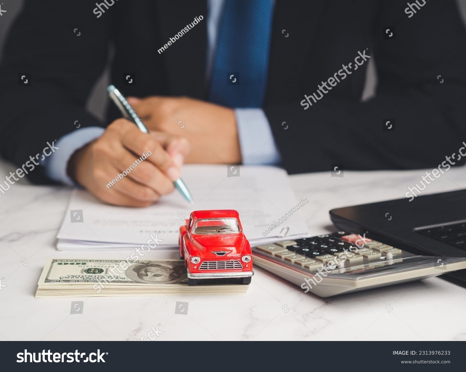 Auto title loan or Car loan. A Businessman signs a contract loan agreement while sitting at the table. Mini a red car model, a calculator, and a laptop on a table. Car finance and insurance concept #2313976233