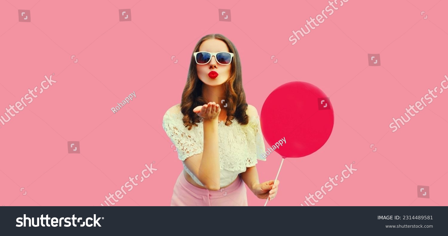 Summer portrait of beautiful young woman blowing her lips sending sweet air kiss with balloon on pink background #2314489581
