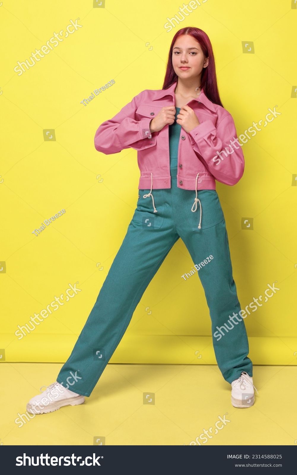 A girl in a pink denim jacket and an oversized emerald jumpsuit on a yellow background studio isolated #2314588025