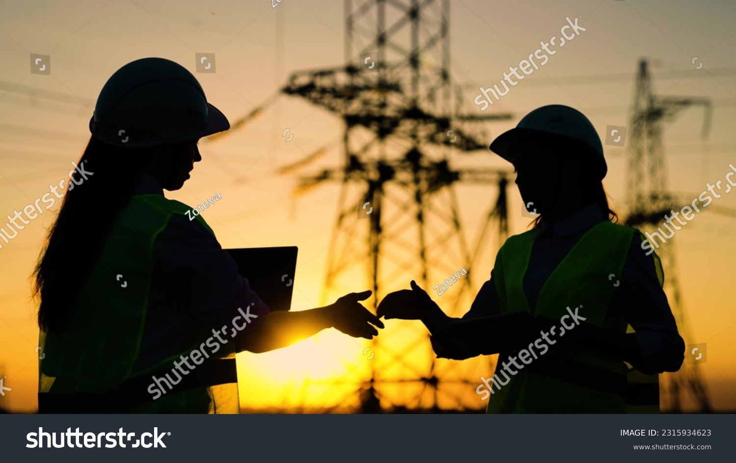 Colleagues women shake hands. Teamwork of power engineers in protective helmets, maintenance of power lines in outdoors. Two construction engineers work together on an electrical transmission line. #2315934623