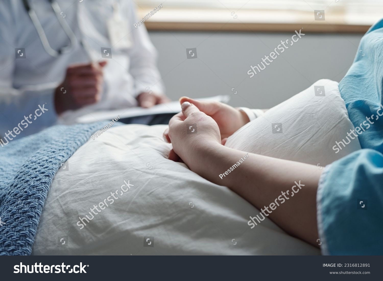Close-up of hands of young woman with oncological disease sitting under blanket in bed and consulting with her doctor after medical treatment #2316812891
