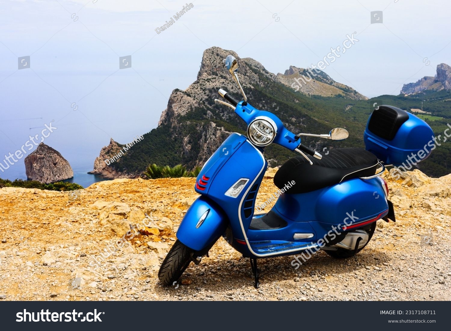 Blue motor scooter on coastal road with sea and rocks in background. High quality photo #2317108711