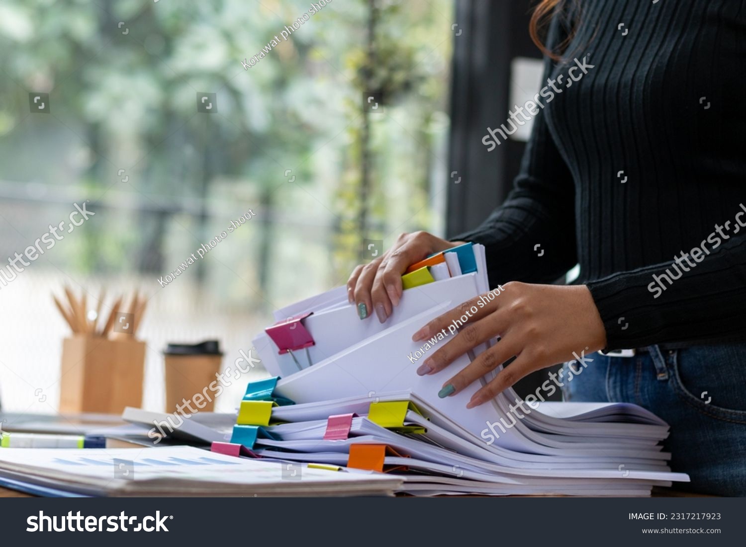 secretary searches through stacked documents on desk in office to find lease within stacked documents just before meeting. concept difficulty in finding hire purchase contract from stacked documents #2317217923