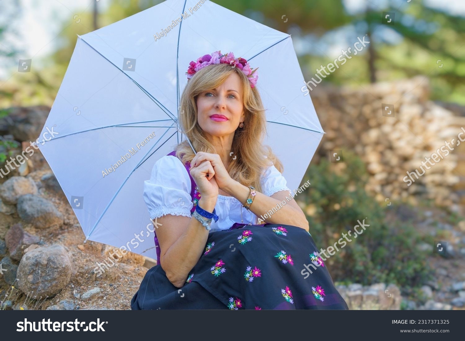 Beautiful woman in typical Austrian costume holds an umbrella on a sunny spring day. #2317371325
