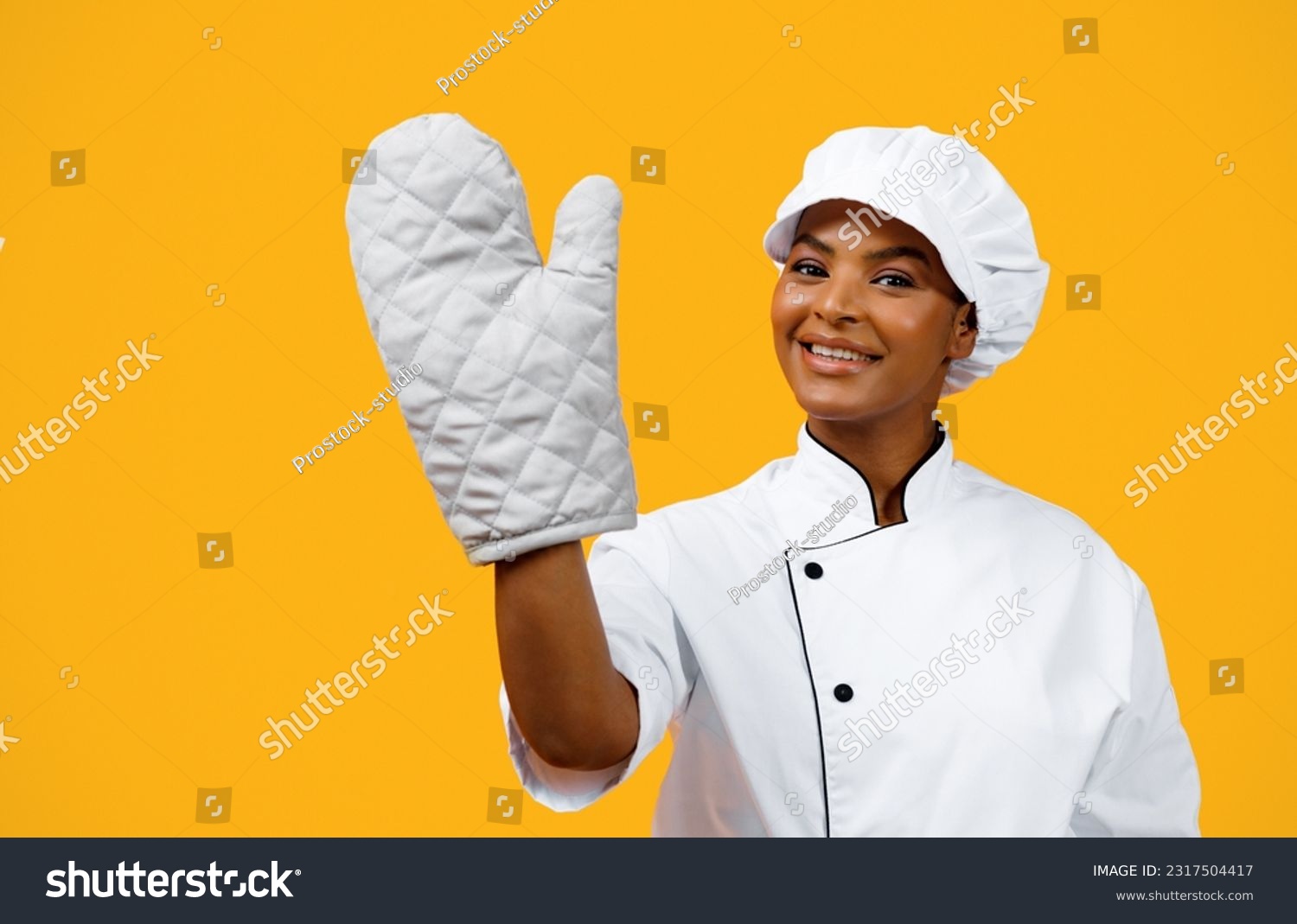 Beautiful Black Female Chef Wearing Oven Mitt Posing Over Yellow Background, Cheerful African American Cooker Lady In Heat Protective Glove And Toque Looking And Smiling At Camera, Copy Space #2317504417