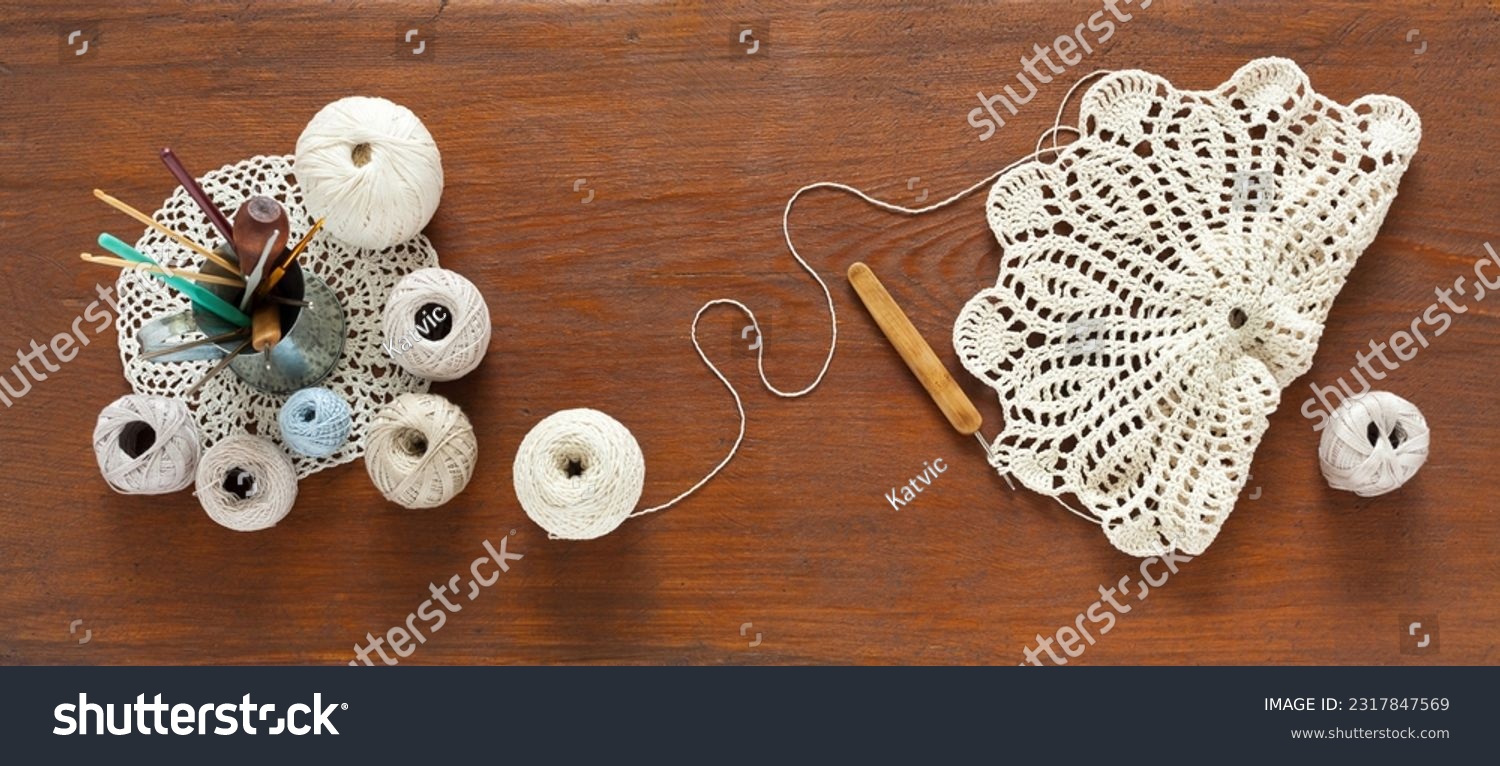 Flat lay of hand crochet lace doily process on wooden background. Set of cotton yarn natural pastel colors and crochet hooks in mug. DIY concept, handmade gifts. Top view, close-up, mock up #2317847569