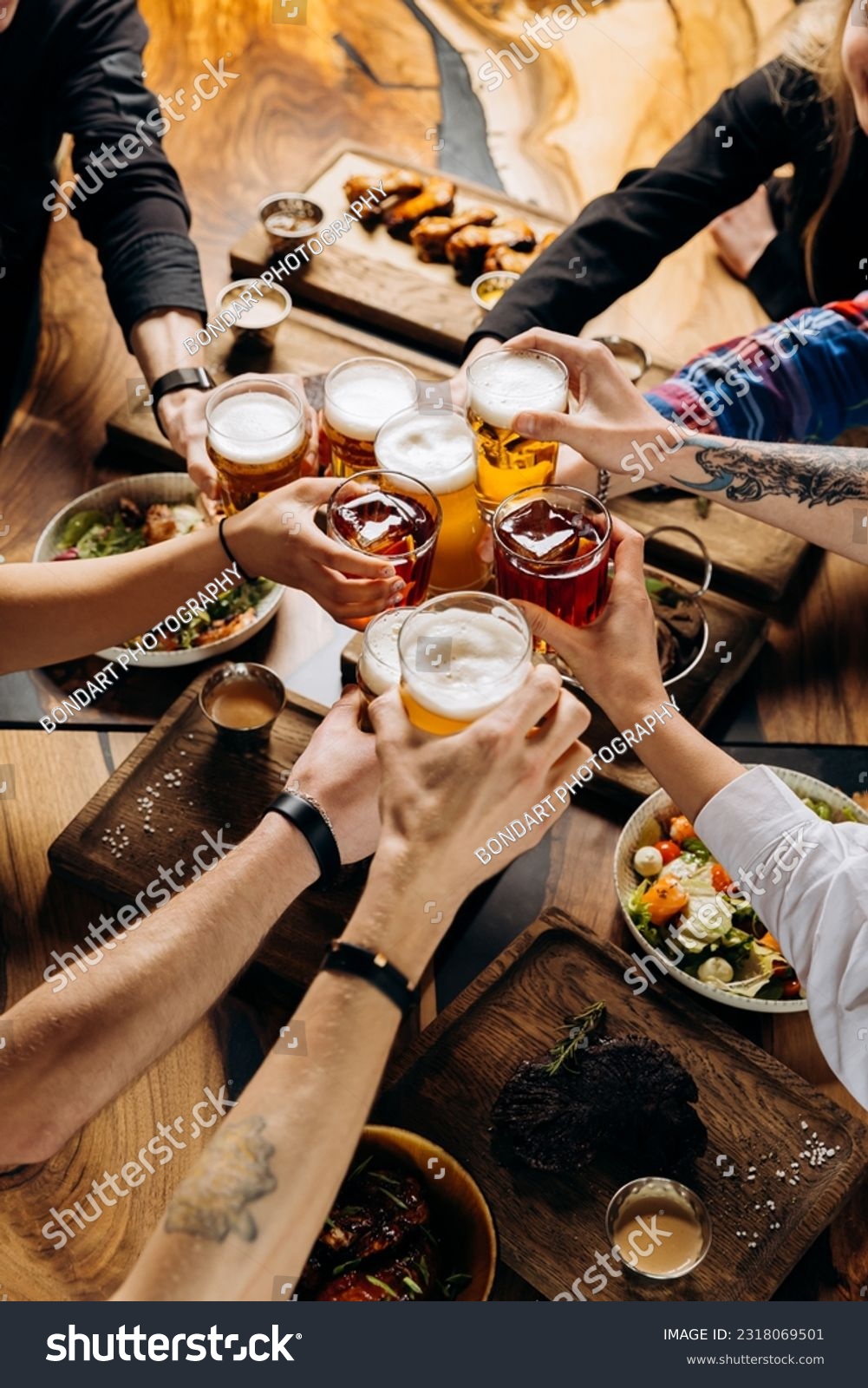 Friends cheering beer glasses on wooden table covered with delicious food - Top view of people having dinner party at bar restaurant - Food and beverage lifestyle concept #2318069501