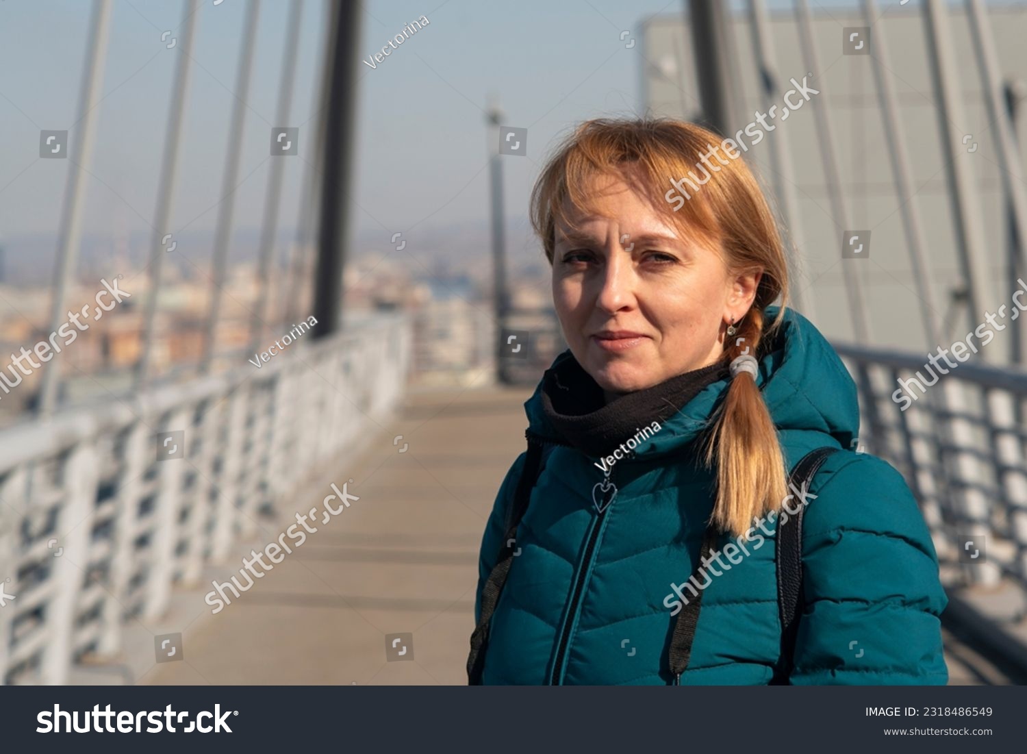 A girl in a green autumn jacket on a bridge on a sunny day. Pedestrian bridge on suspension ropes. #2318486549