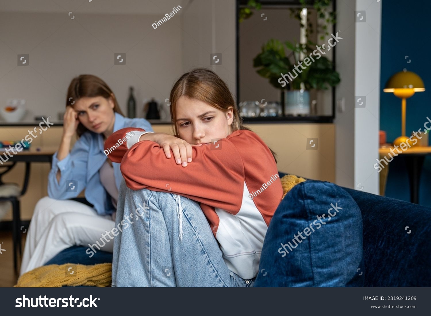 Frustrated teenage girl sits hugging his knees, looks away. Mom sits next daughter and comforts after quarrel. Communication problems between parent and kids.Ignoring children problems.Bulling school #2319241209