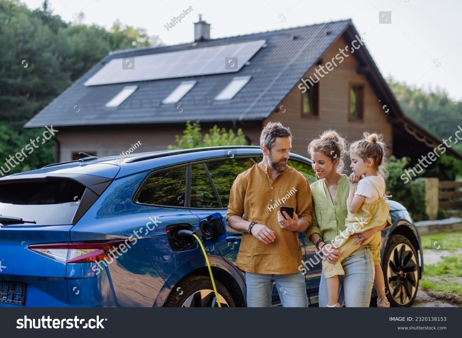 Family with little girl standing in front of their house with solar panels on the roof, having electric car. #2320138153