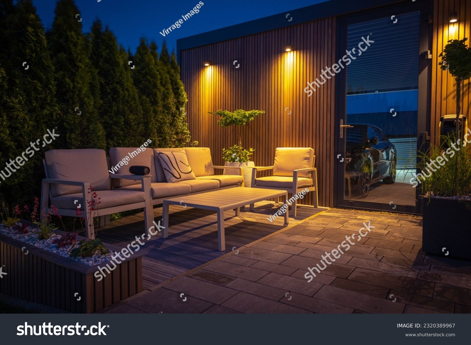 Lounge and Dining Area at Modern Residential Backyard Decorated with Outdoor Lights, Plants, Garden Table and Chairs. Cozy Summer Evening. #2320389967