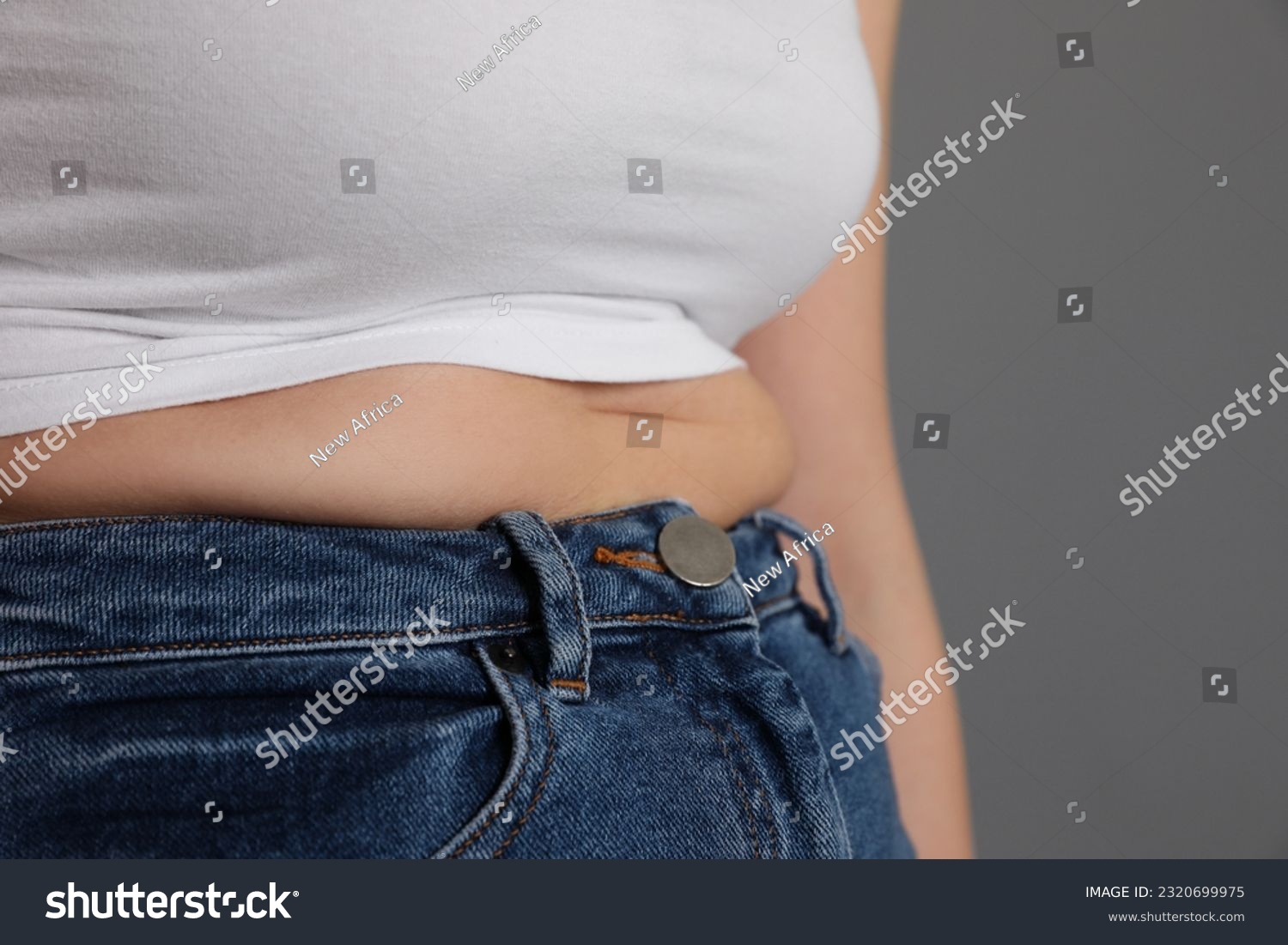 Overweight woman in tight shirt and jeans on grey background, closeup. Space for text #2320699975