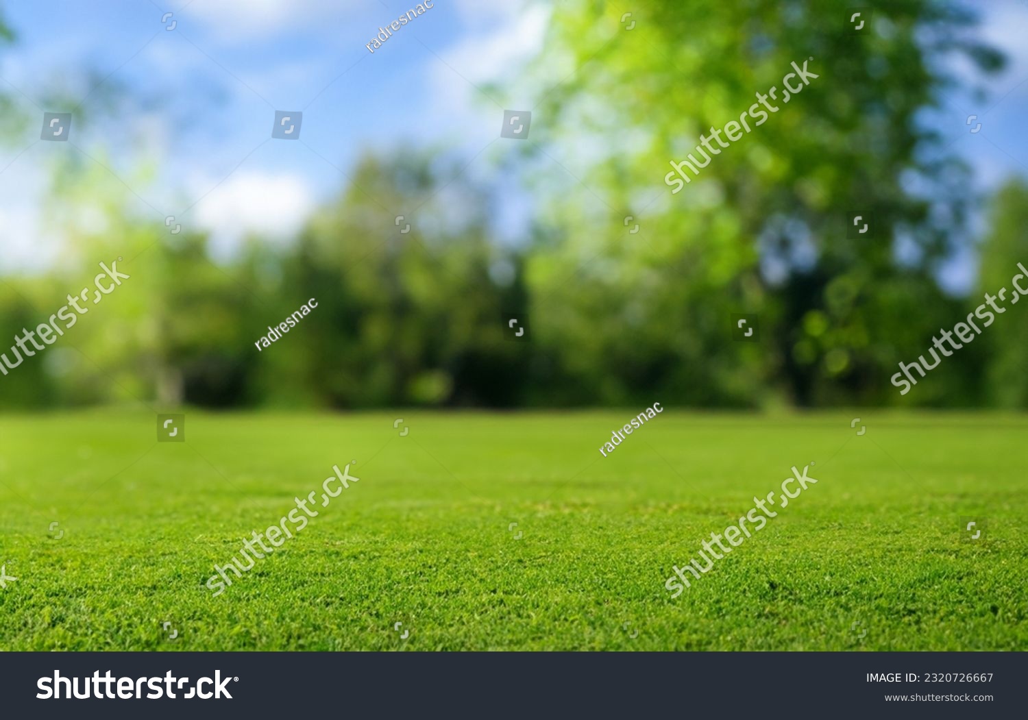 Beautiful blurred background image of spring nature with a neatly trimmed lawn surrounded by trees against a blue sky with clouds on a bright sunny day. #2320726667