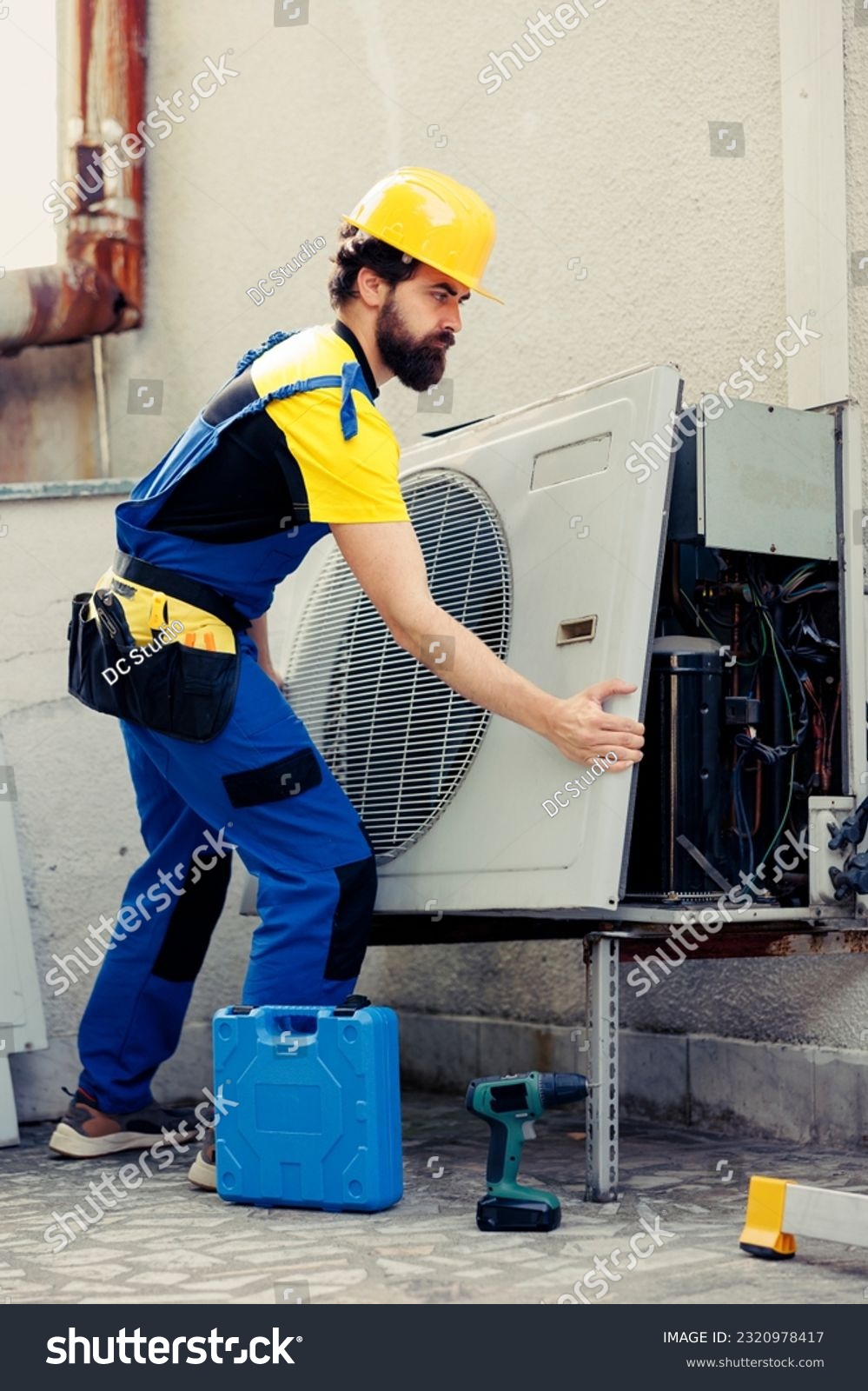 Licensed expert starting work on out of order air conditioner, using power tool to dismantle condenser metal coil panel. Skilled wireman opening hvac system to check for bad wiring #2320978417