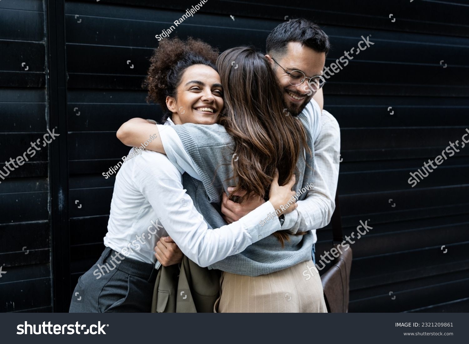 Cheerful businessman and businesswomen hugging each other in front of office building. Colleagues hug colleague who change her job and work, going to another company. #2321209861