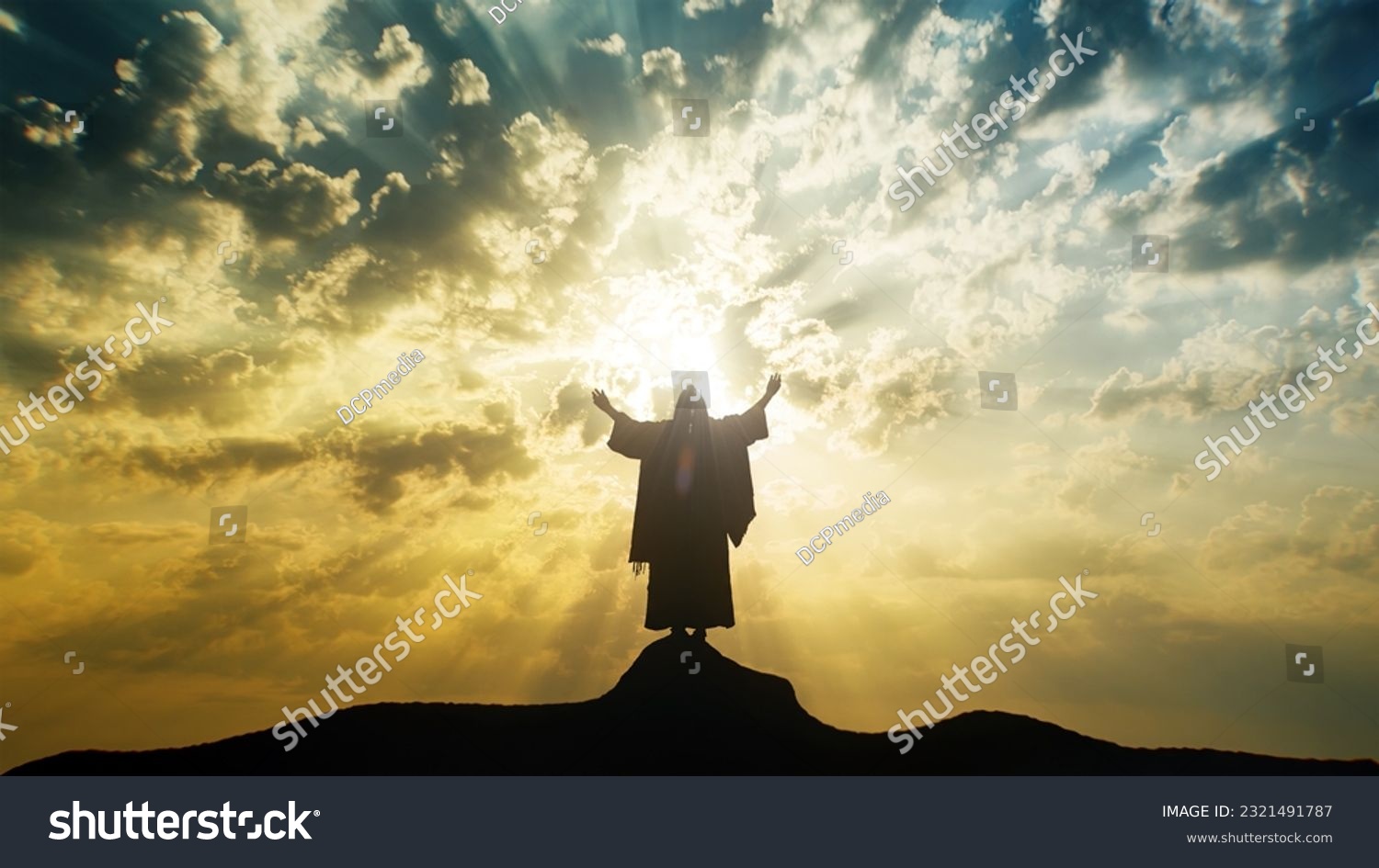 Silhouette of Jesus praying with raised hands on a mount with mystic clouds behind Him. #2321491787