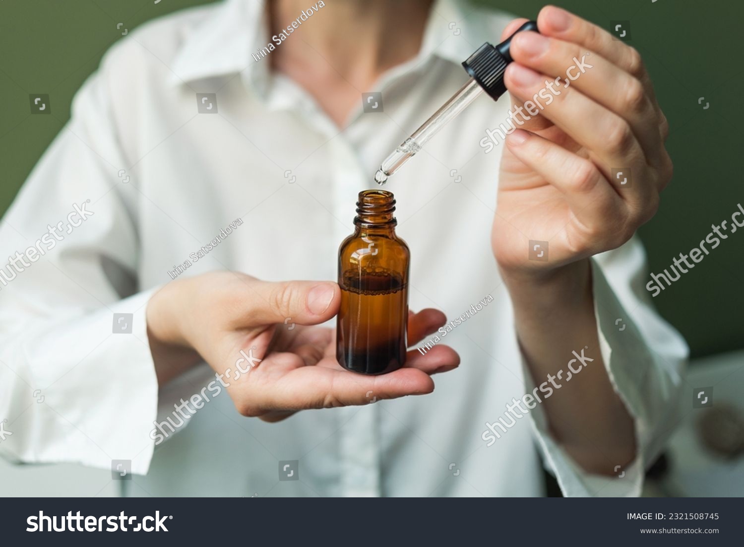 Essential oil with a pipette in the hands of a woman on a green background. Women's hands with a bottle of oil and a pipette - the sphere of beauty #2321508745