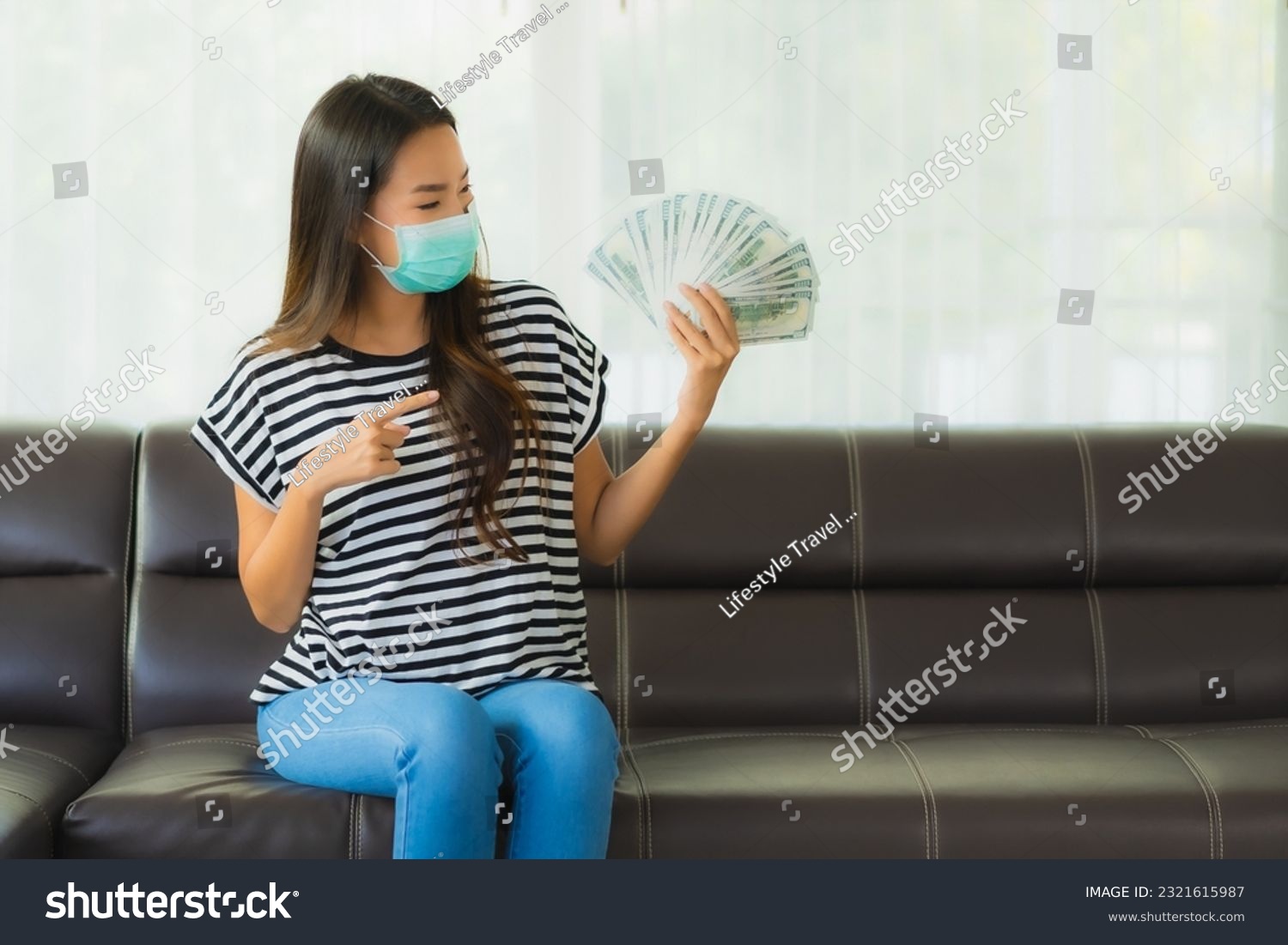 Portrait beautiful young asian woman with mask on sofa show money or cash at home #2321615987