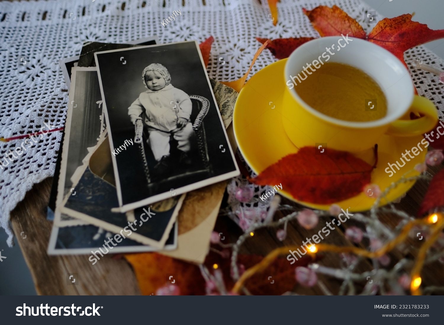 old vintage monochrome photographs scattered on rustic wooden table, Autumn composition with hot tea in mug, fallen yellow, orange leaves, concept family tree, genealogy, cozy autumn mood #2321783233