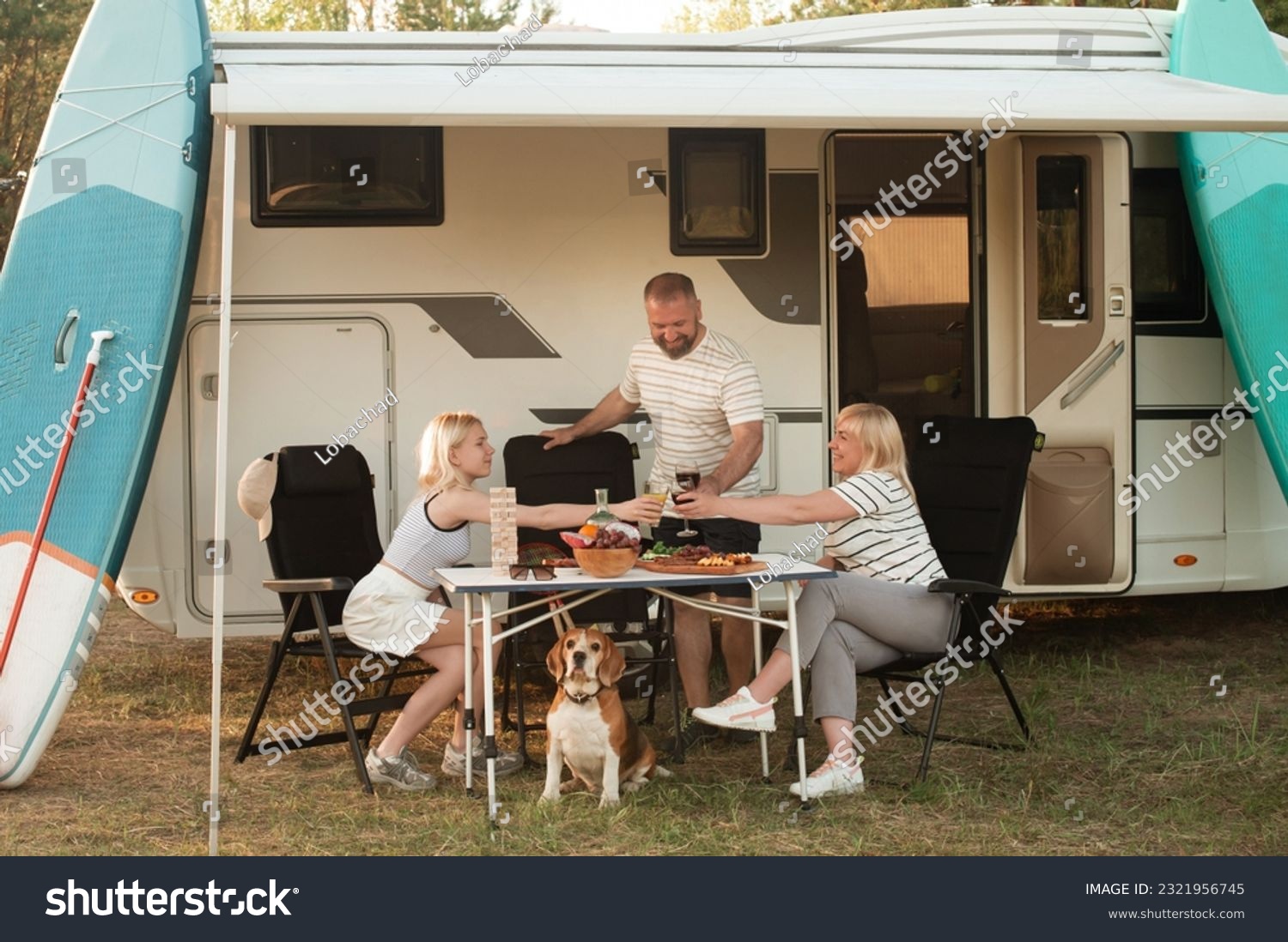A happy family is resting nearby near their motorhome in the forest. #2321956745