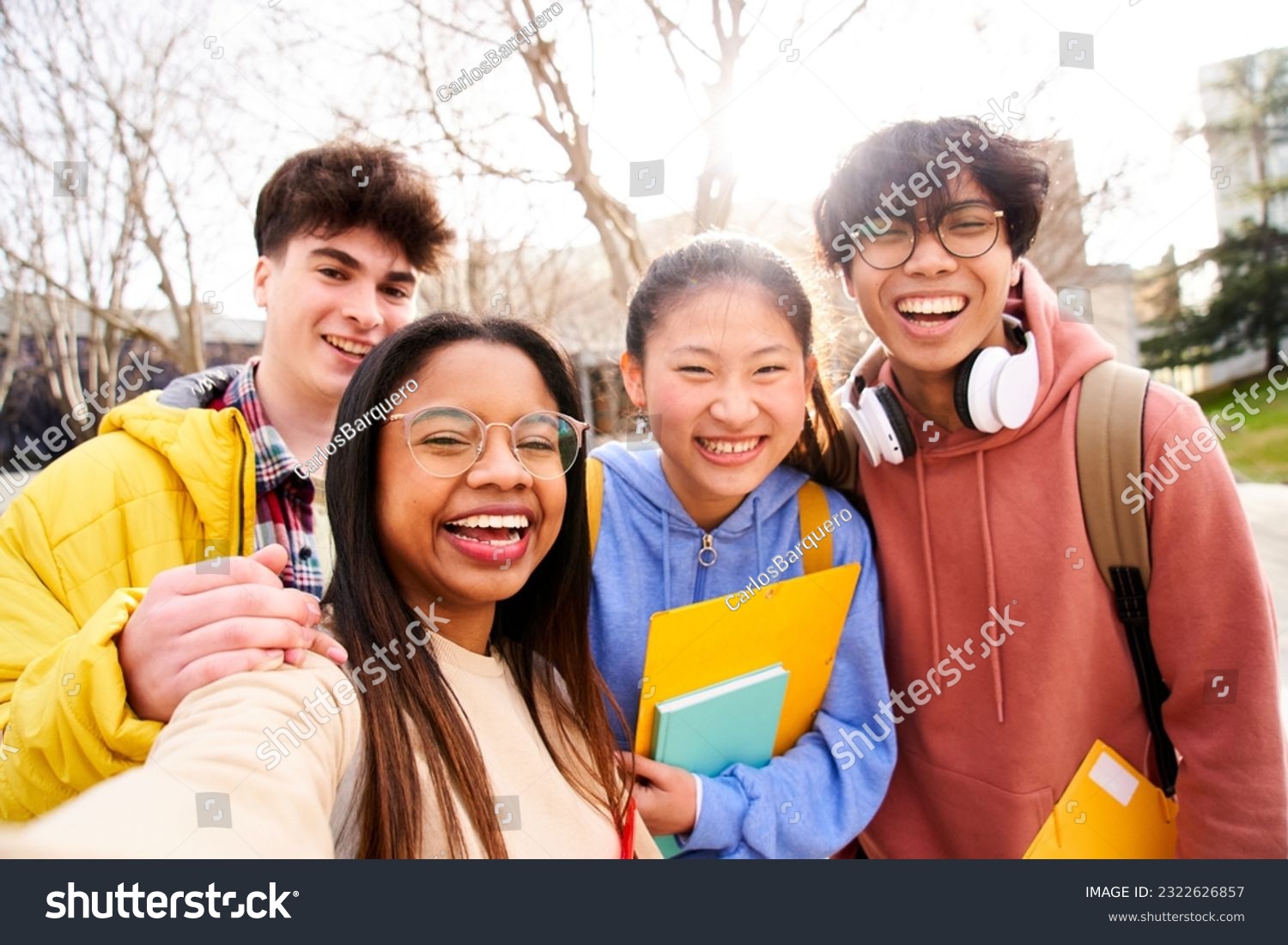 Group of multi-ethnic high school students taking a selfie outdoors at the university campus holding folders. Looking at camera picture of a diverse colleagues having fun.  #2322626857
