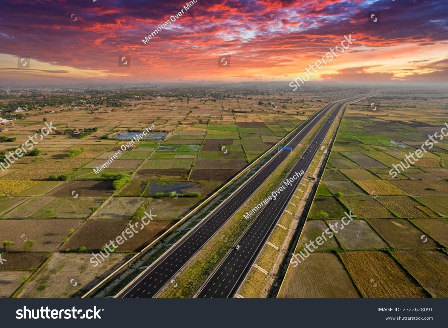 locked tripod aerial drone shot of new delhi mumbai jaipur express elevated highway showing six lane road with green feilds with rectangular farms on the sides #2322628091